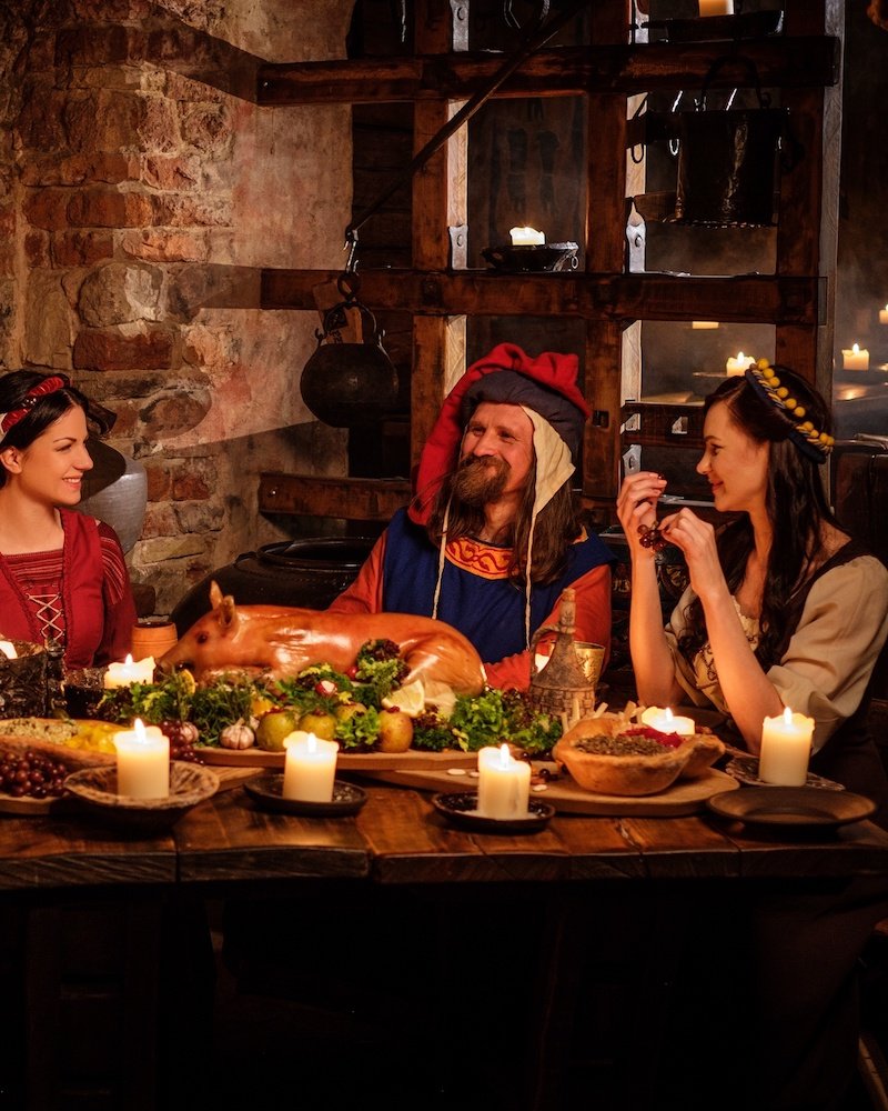 Medieval people eat and drink in ancient castle kitchen interior.